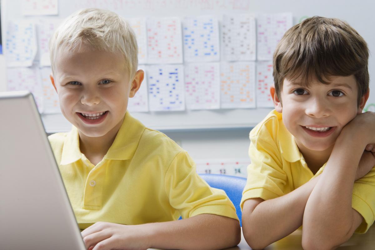 Zwei Grundschulkinder mit gelben T-Shirts arbeiten am PC und lächeln in die Kamera. Foto: © shutterstock - bikeriderlondon